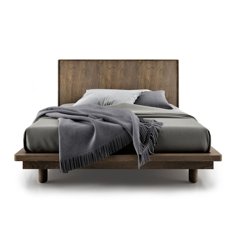 A bed with a dark brown wooden frame and headboard, featuring a gray blanket and pillows.