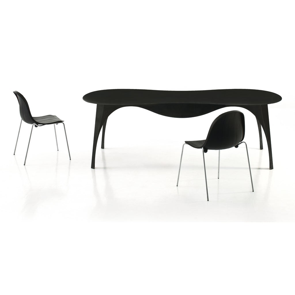 A sleek black oval dining table with curved white legs, accompanied by black chairs in a minimalist setting.