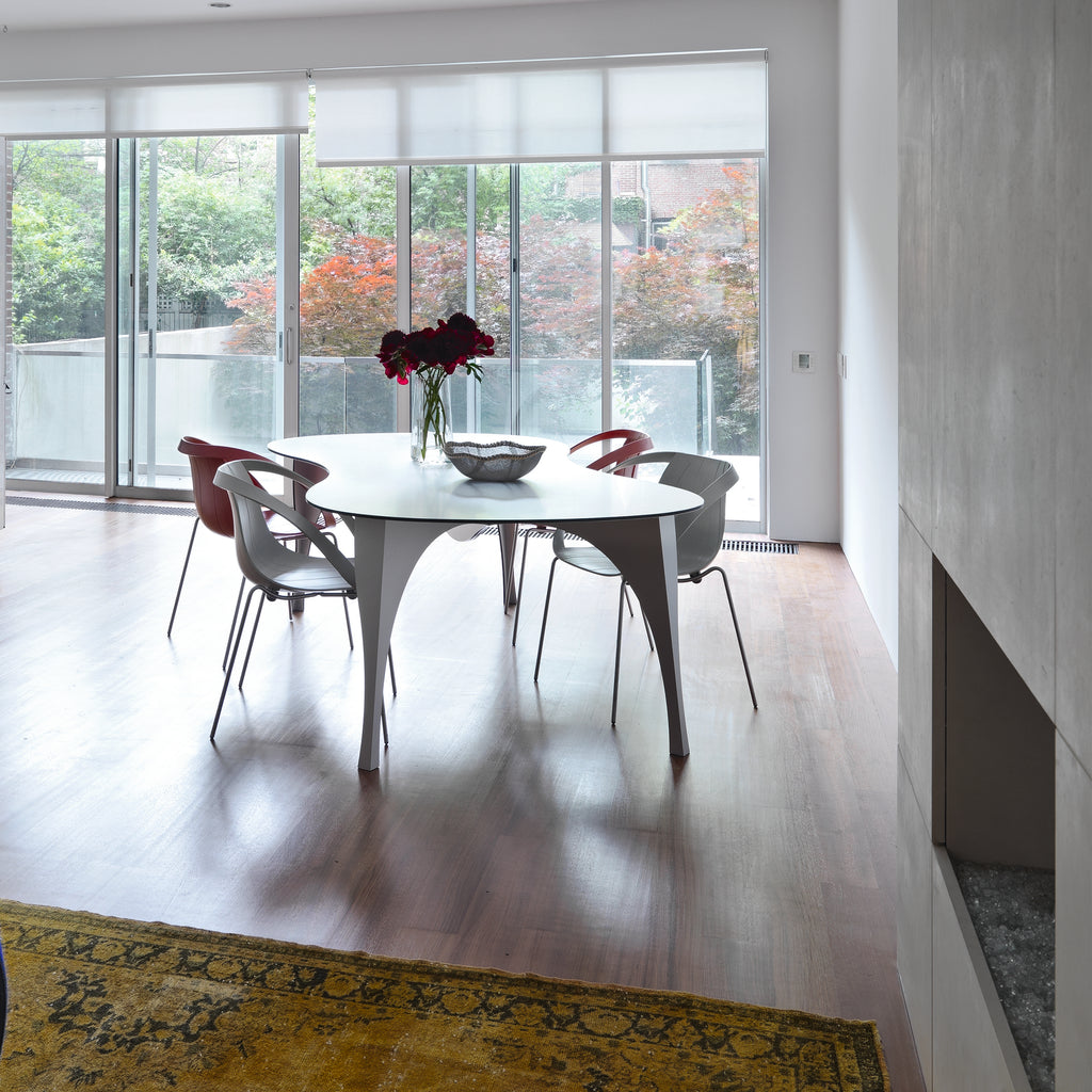 Dining area in a bright room with a white oval table and gray chairs around it.