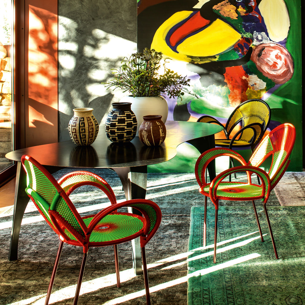 Colorful indoor scene with red and green chairs around a dark table and vibrant wall art.