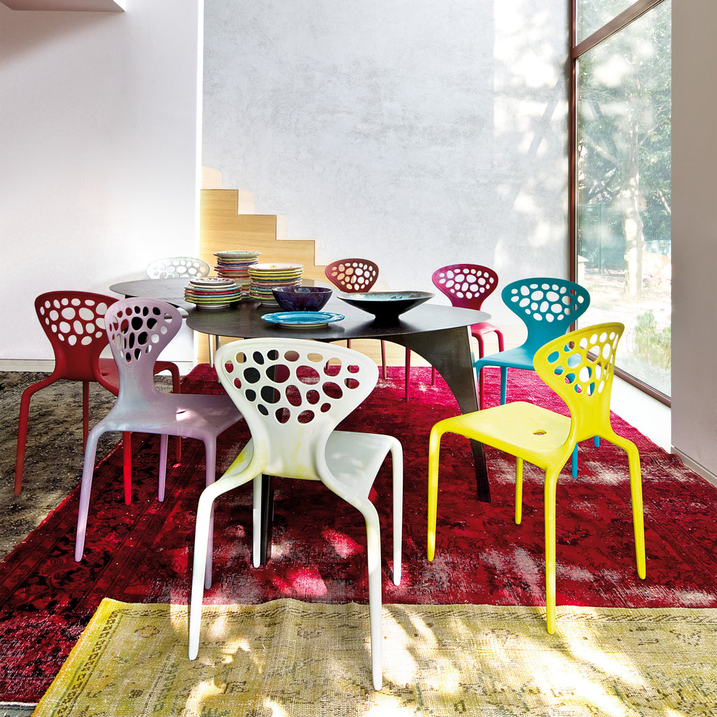 Indoor dining with a black oval table and colorful chairs on a bright red and yellow rug.