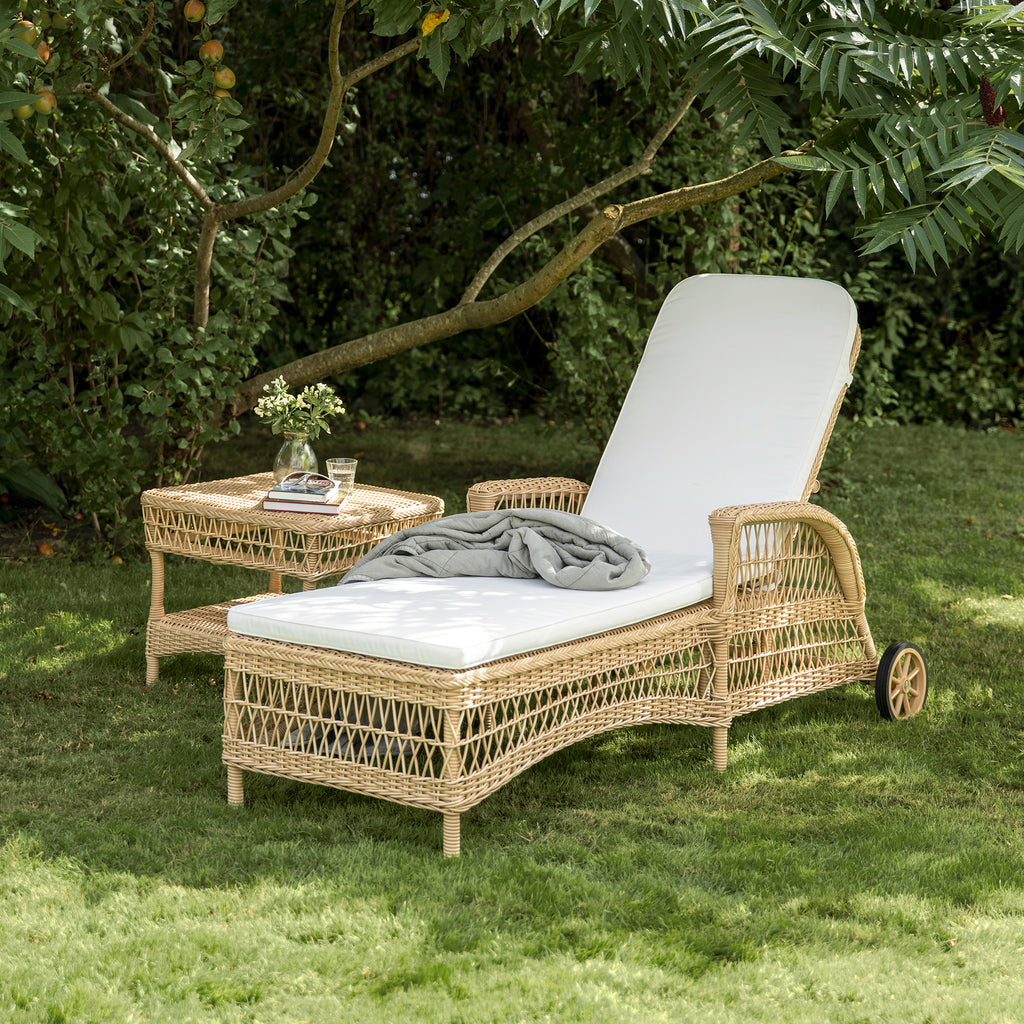 Wicker outdoor lounge chair with white cushion and gray blanket.