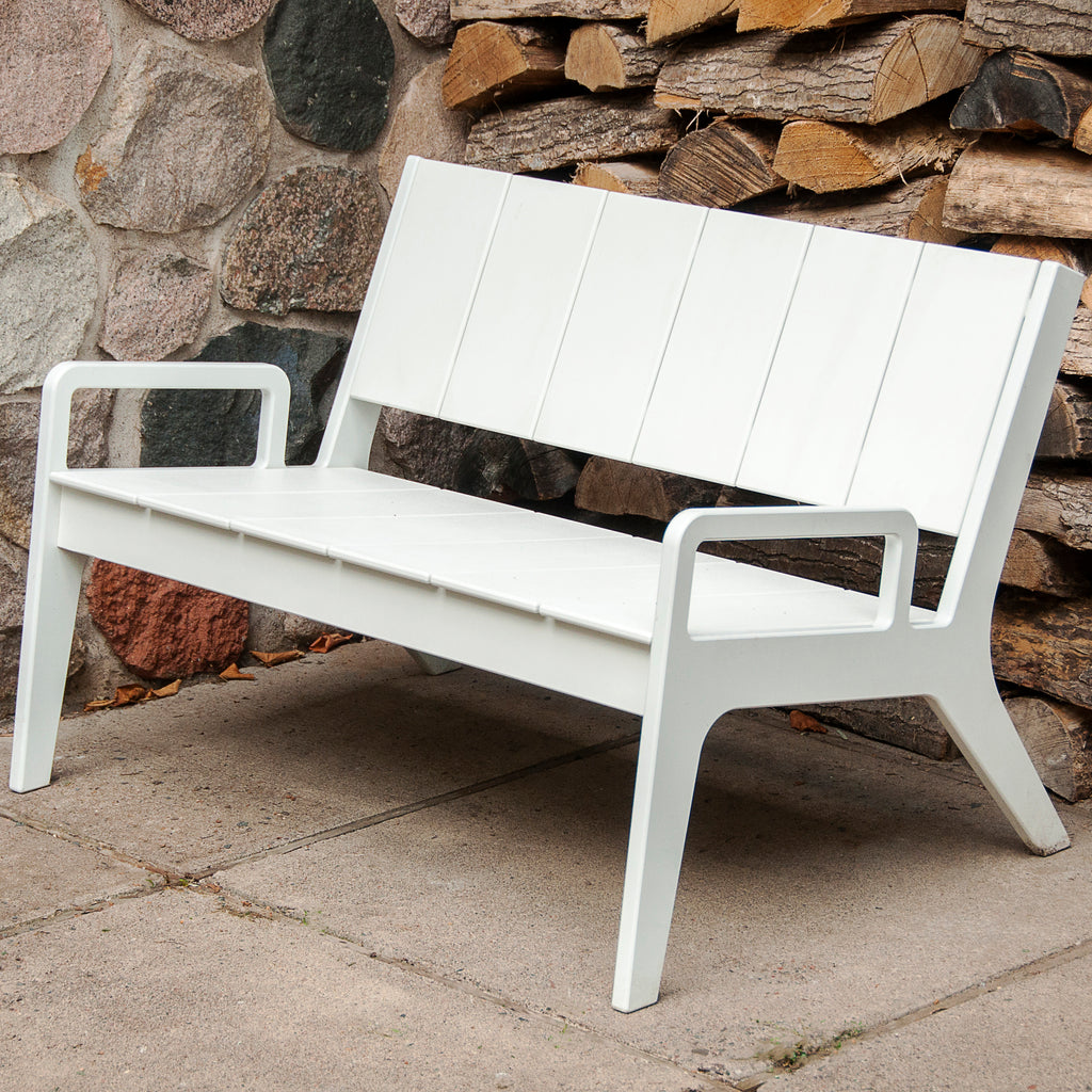 White outdoor bench with matching back and arms against stone wall